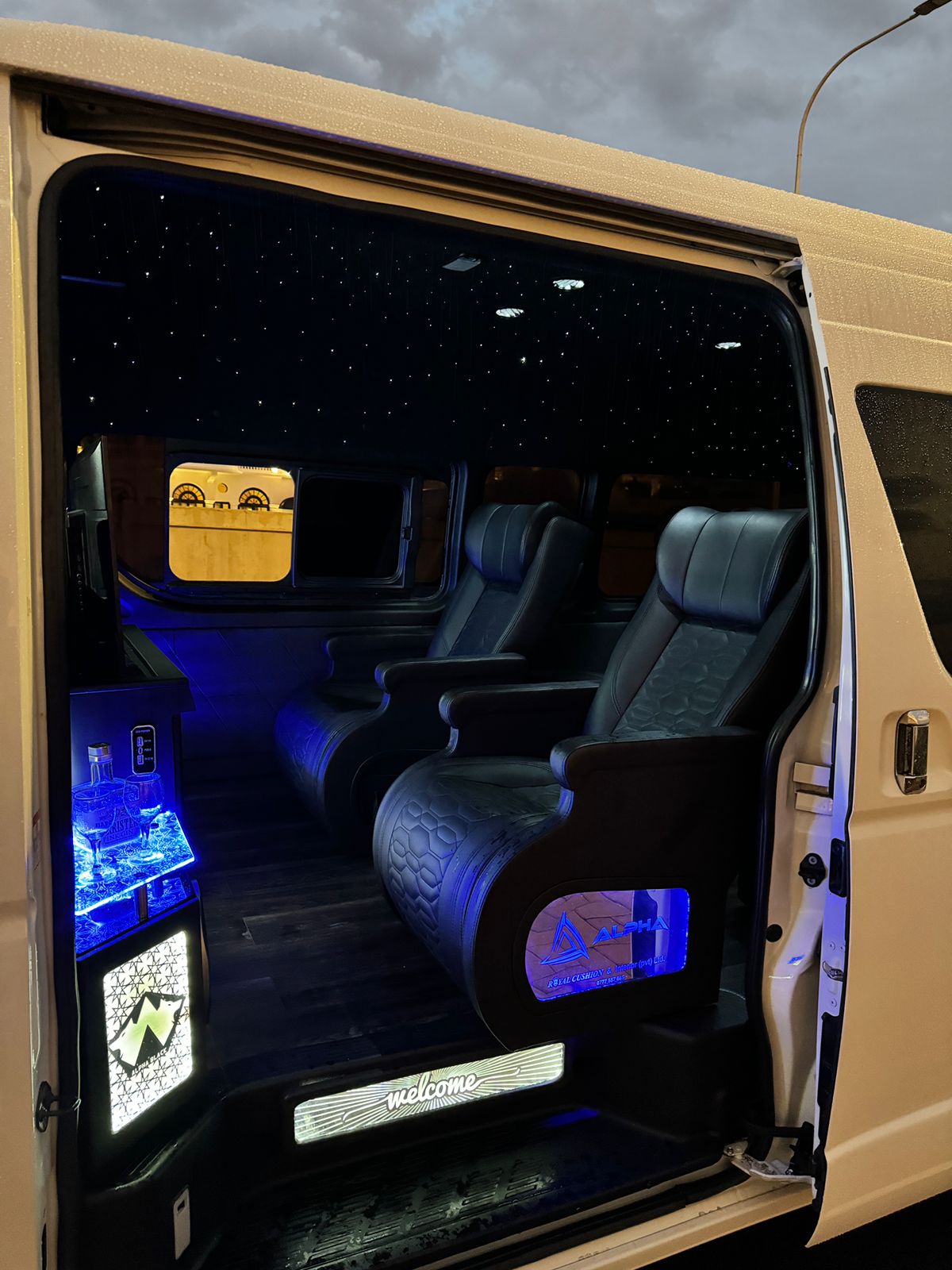Open side door of the van showing lit welcome step and mini bar